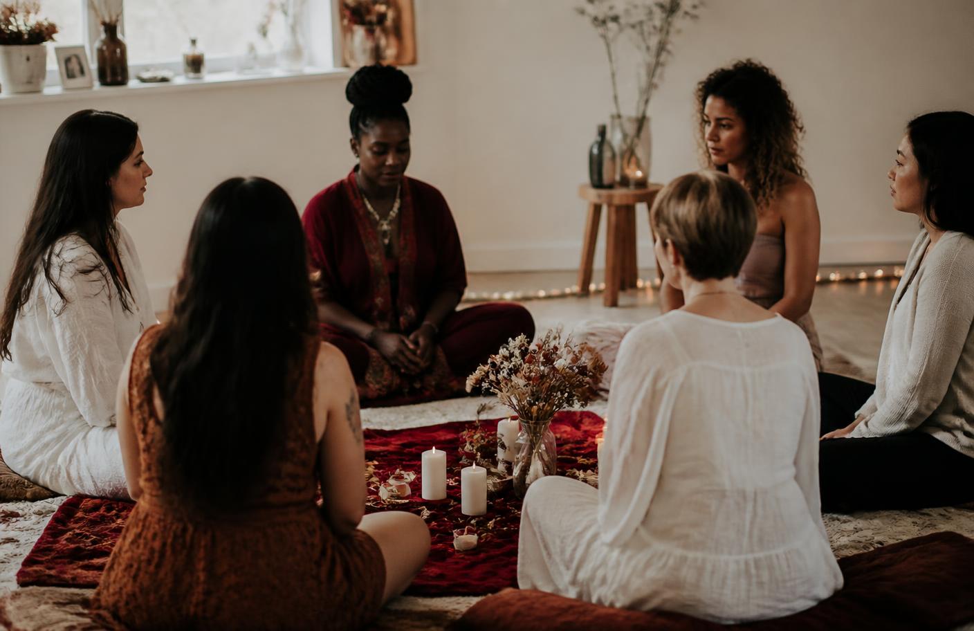 Círculo de mulheres sentadas em roda em uma sala clara com velas e tecidos vermelhos